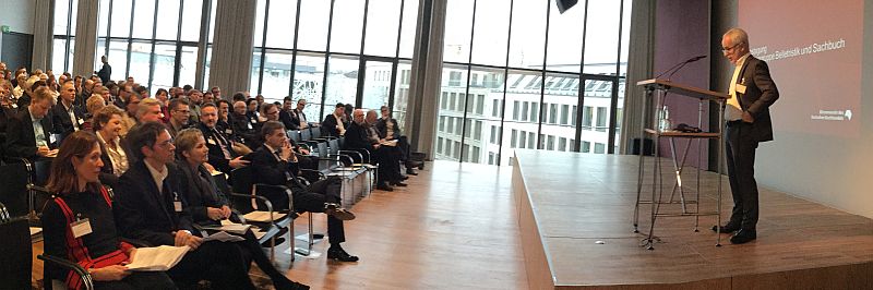 Die IG Belletristik und Sachbuch tagt in München. Das Foto (buchreport/Thomas Wilking) zeigt Börsenvereins-Vorsteher Heinrich Riethmüller bei seinem Grußwort. Vorne links sitzen in der ersten Reihe die Sprecher der IG (v.l.): Felicitas von Lovenberg (Piper Verlag), Andreas Rötzer (Matthes & Seitz), Annette Beetz (Verlagsgruppe Random House).
