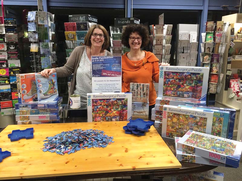 Lesezeichen Germering: Mit ihrer Puzzle-Spendeaktion für einen sozialen Zweck wollen die Buchhändlerinnen Katrin Schmidt und Helen Hoff (v.l.) einen engagierten Verein unterstützen und zugleich neue Zielgruppen ansprechen. Mit der überregionalen Aufmerksamkeit nicht nur unter den Kollegen, sondern auch in der Presse hätten sie aber nicht gerechnet, meint Katrin Schmidt: „Die Presse liebt einfach solche Geschichten über Kooperationen.“ (Foto: Buchhandlung Lesezeichen)